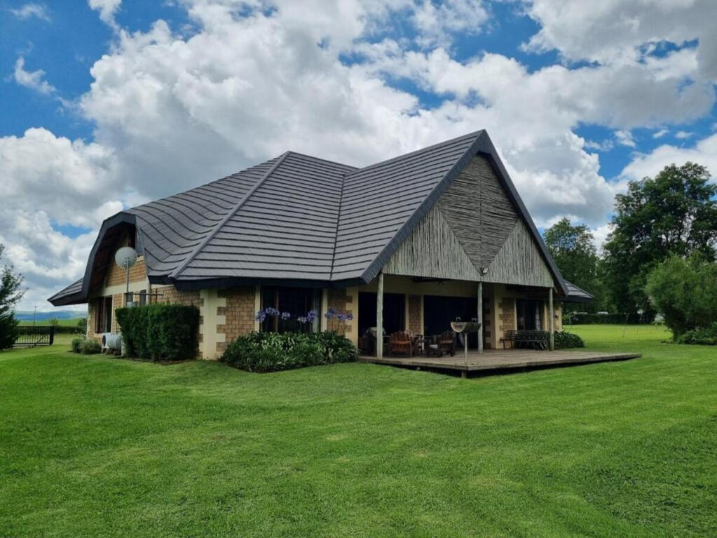 Plain Champagne Guest Farm Homestead Exterior Exterior view of the Plain Champagne Guest Farm homestead with thatched roof and wide green lawn in the Drakensberg